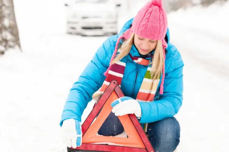kobieta na ośnieżonej drodze ustawia trójkąt ostrzegawczy