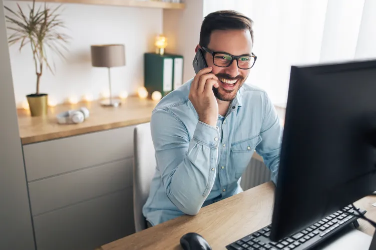 mężczyzna rozmawiający przez telefon przed ekranem komputerowym 